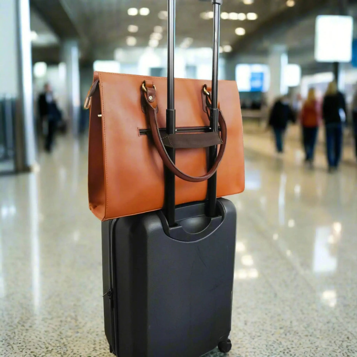 Tan 17-inch Signature bag secured to a rolling suitcase at an airport